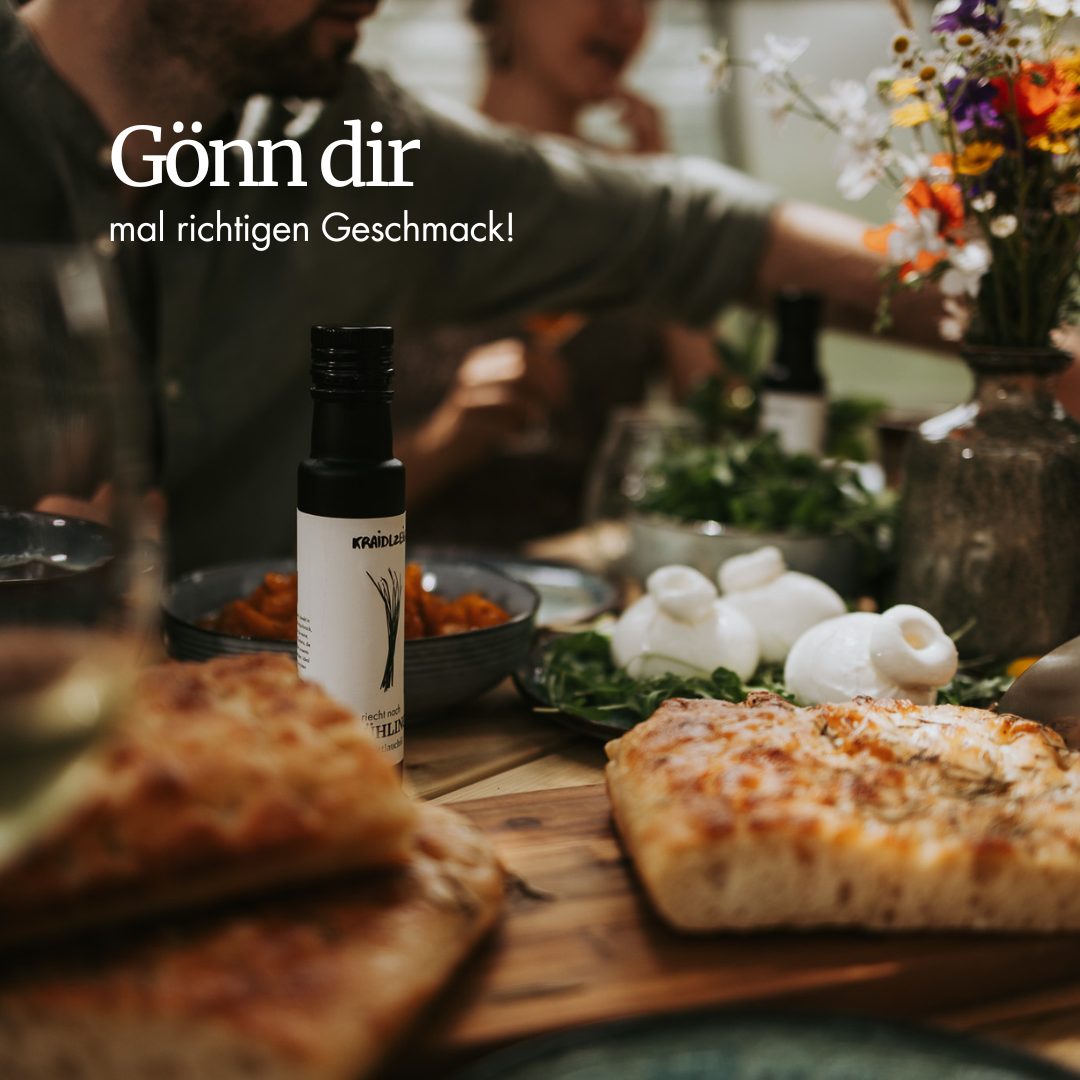 Flasche Kräidlzeig Bio-Schnittlauchöl auf einem gedeckten Tisch mit Brot, frischen Kräutern und Freunden – natürliches, regionales Kräuteröl voller Geschmack.